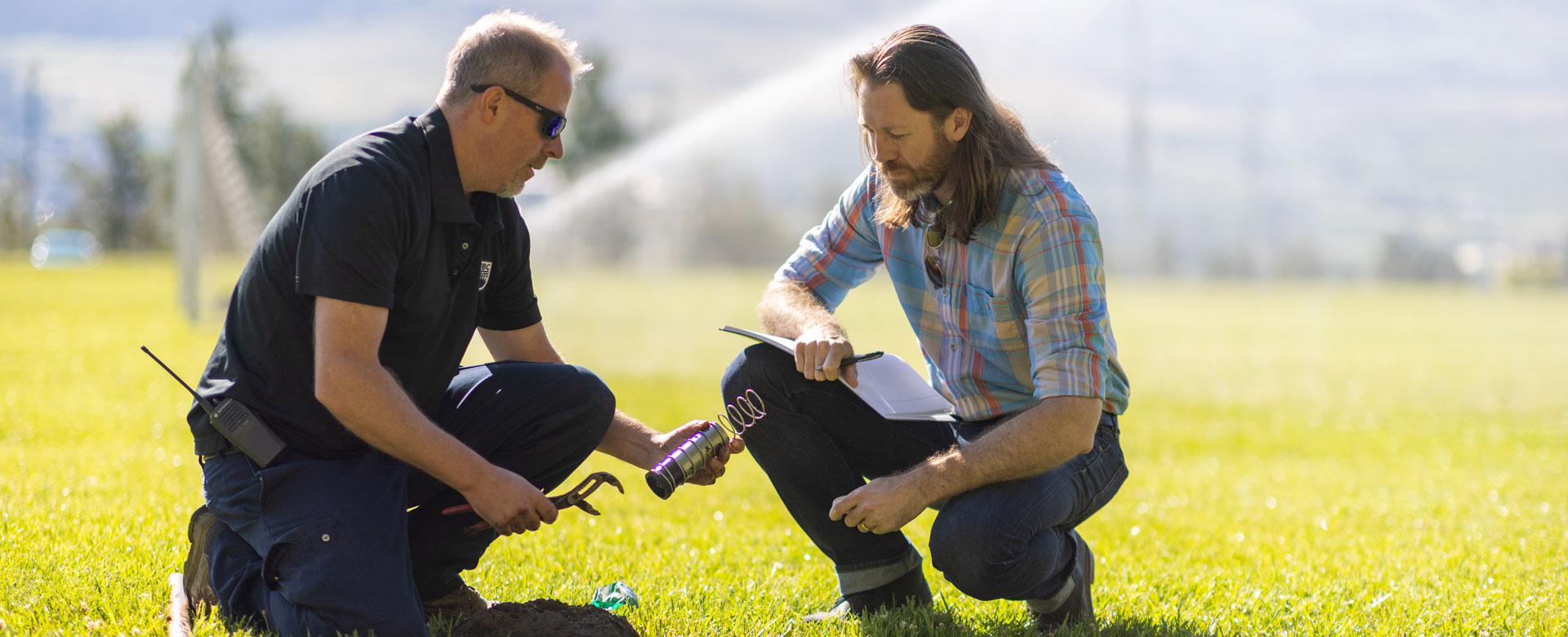 UBC Okanagan Campus Operations and Risk Management staff members standing in a grassy field with a sprinkler on behind them.