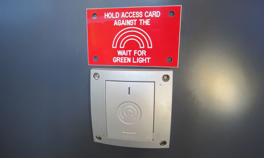 A wall-mounted Salto hotspot with a sign reading "hold access card against the panel, wait for green light".